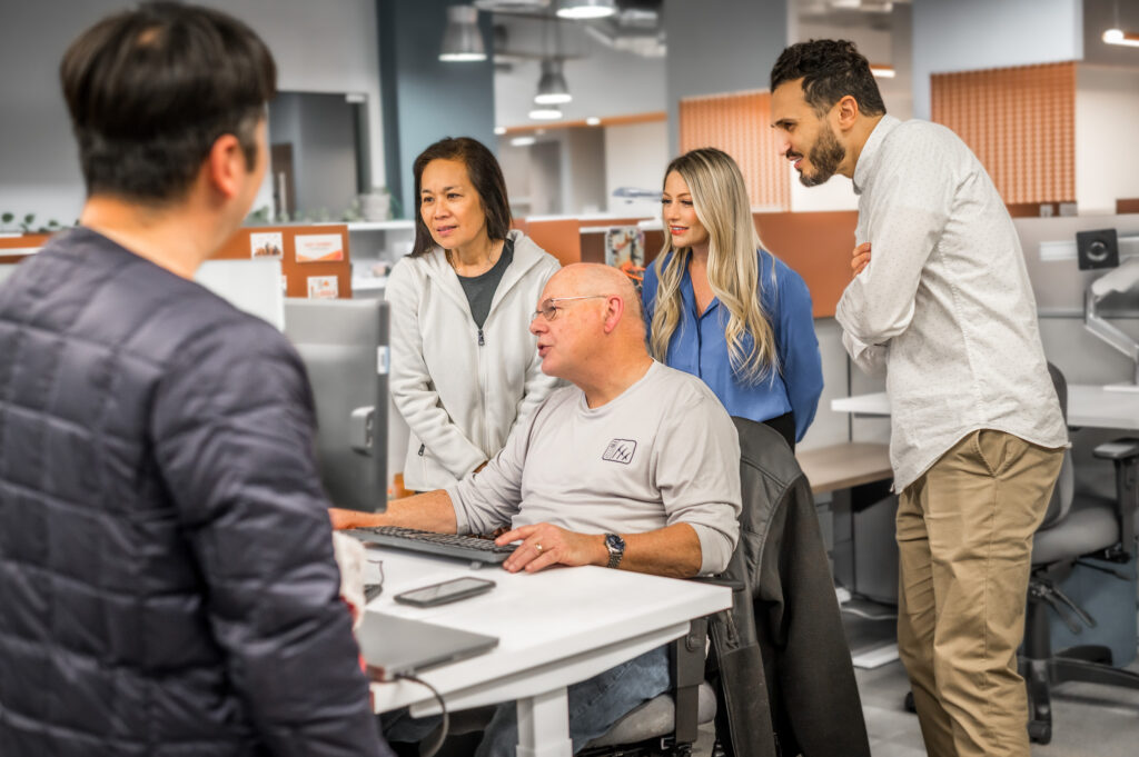 Group of Proponent employees inquisitively looking over the shoulder of a man on his computer