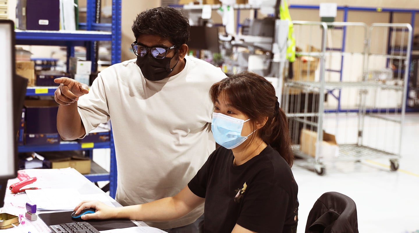 Two people in Singapore office work at a computer wearing masks