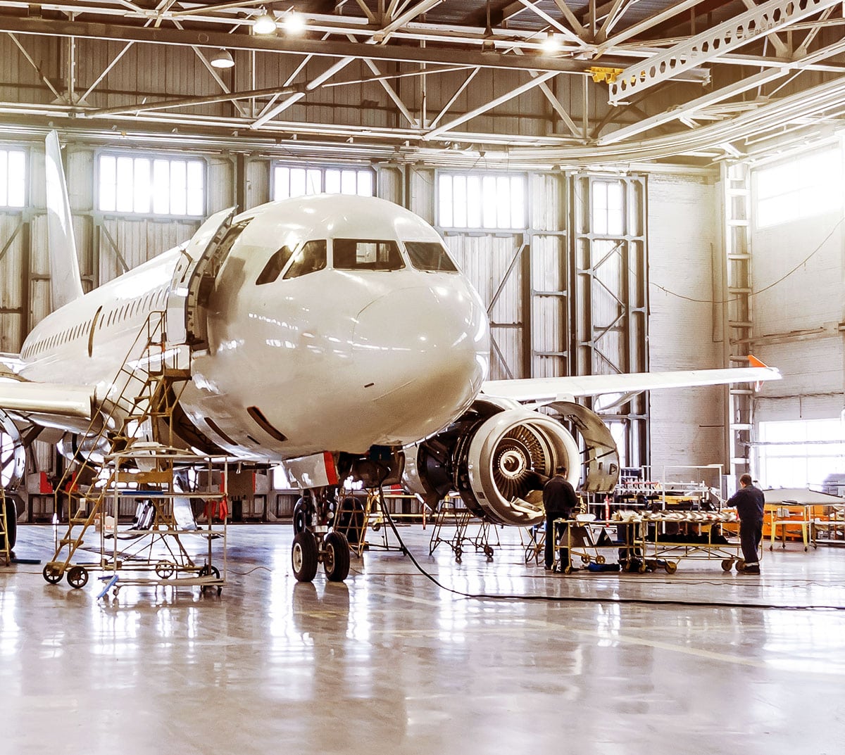 White jet engine plane, being worked on in a hanger by two mechanics.